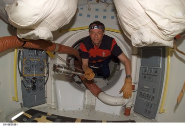 Christer Fuglesang holds a tool as he floats through a hatch on Space Shuttle Discovery